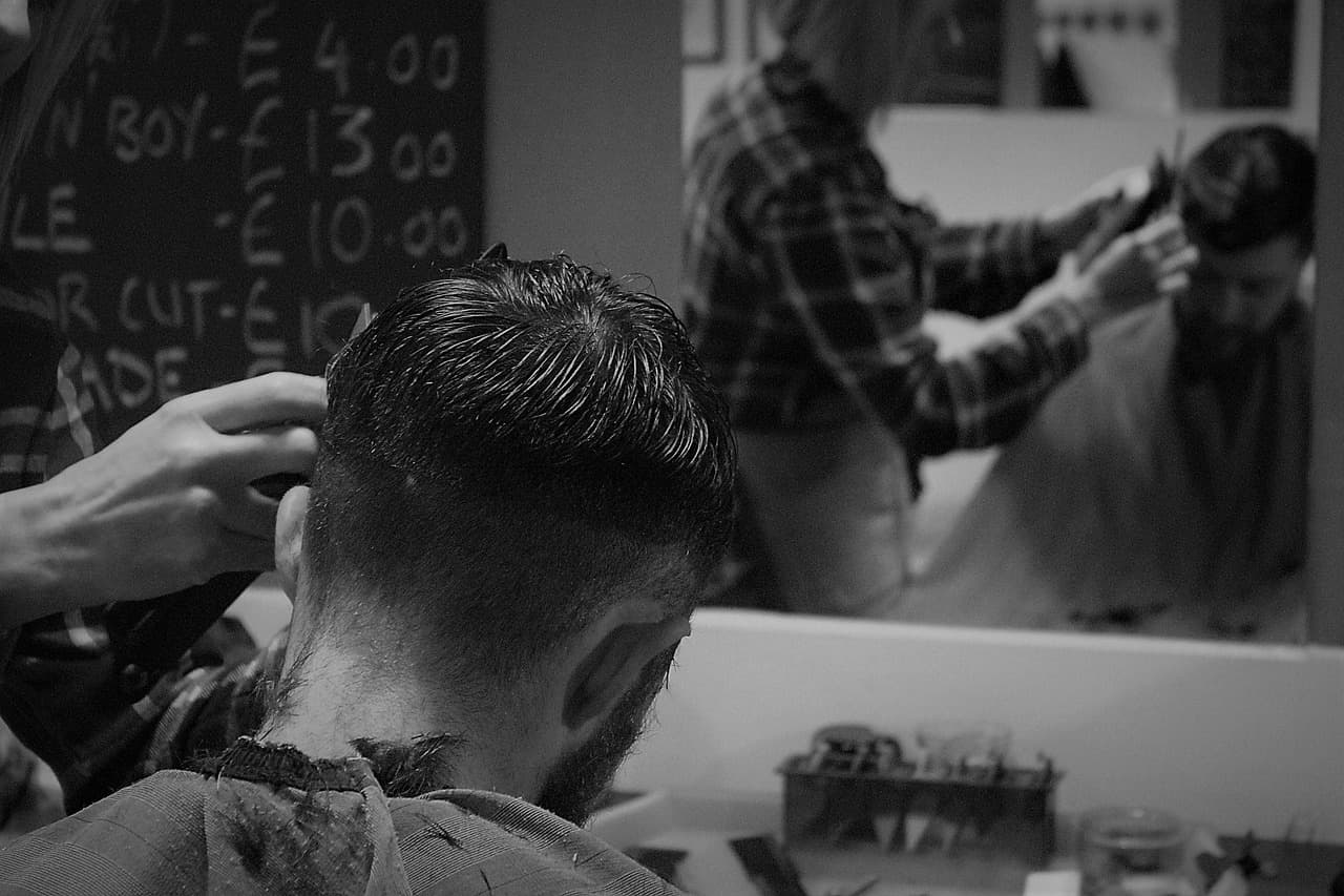 A barber running clippers up the back of a customer's head, in black and white