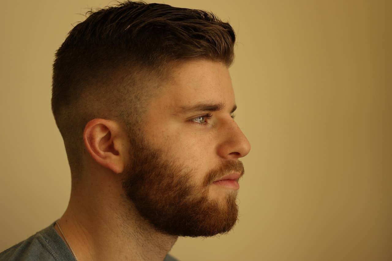 A man in profile with a short fade and a neatly lined beard