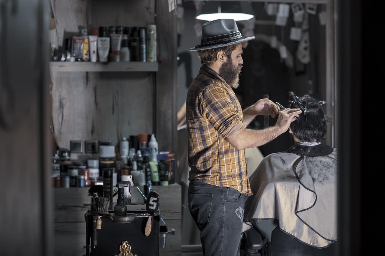 A barber in a hat at work by the shelves of a small barber shop