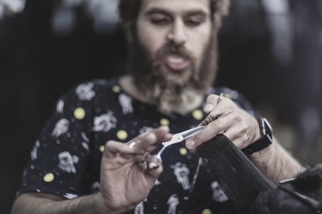 A bearded barber cutting hair with scissors and a comb